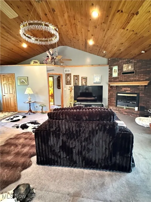 Living room featuring lofted ceiling, carpet, wooden ceiling, a fireplace, and a ceiling fan