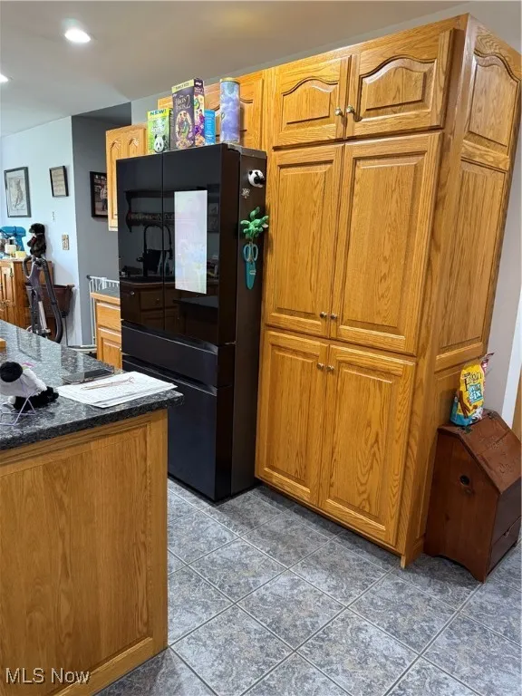 Kitchen with recessed lighting, tile patterned floors, dark stone countertops, refrigerator, and brown cabinetry
