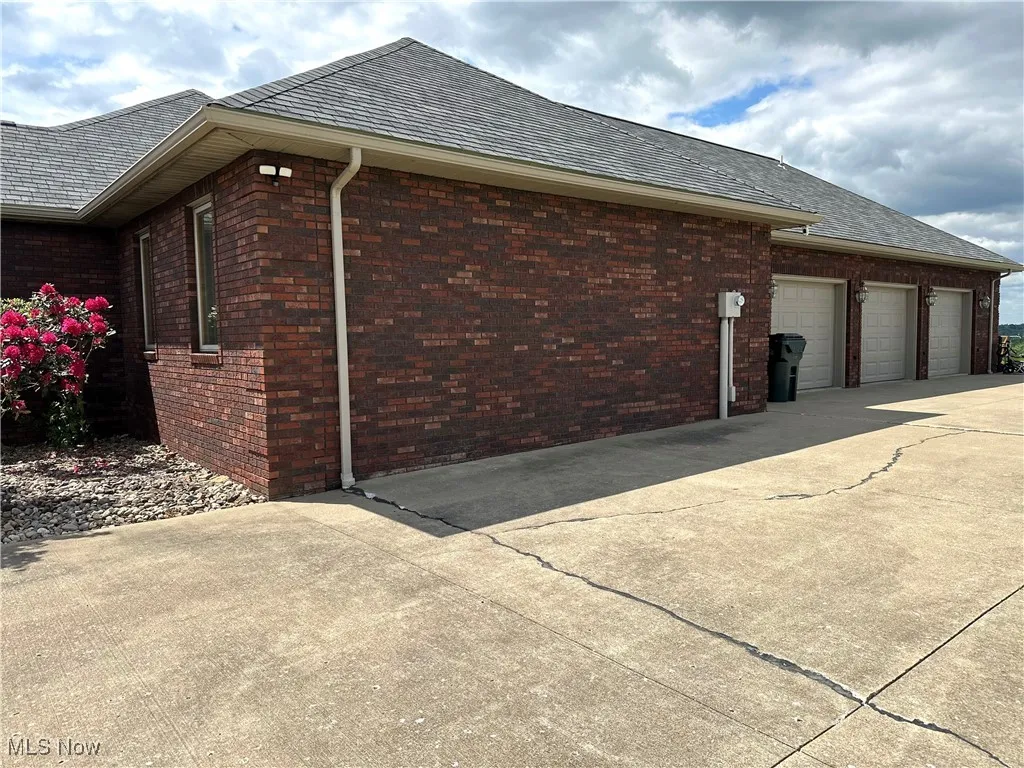 View of side of home featuring brick siding, concrete driveway, an attached garage, and roof with shingles