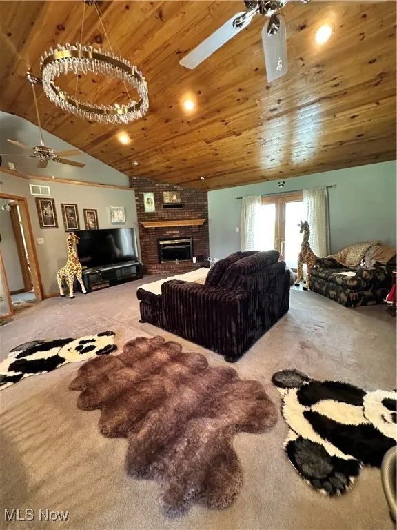 Carpeted living room featuring ceiling fan, vaulted ceiling, wood ceiling, and a fireplace
