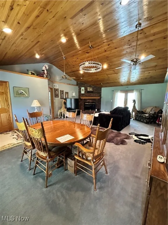 Carpeted dining space featuring a ceiling fan, lofted ceiling, a fireplace, and wooden ceiling
