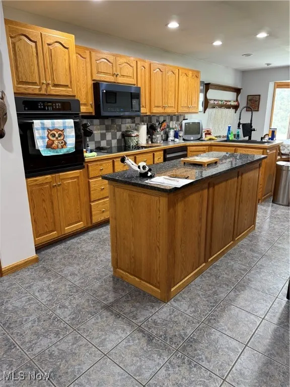 Kitchen with brown cabinets, oven, dark stone countertops, stovetop, and a kitchen island