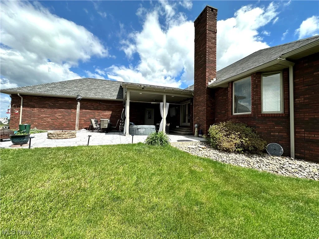 Back of property with a chimney, a yard, brick siding, a patio, and roof with shingles