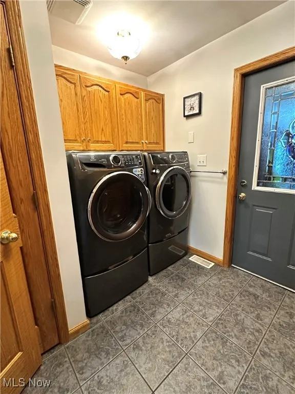 Laundry room featuring cabinet space, washing machine and dryer, dark tile patterned flooring, and baseboards