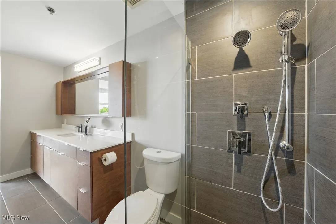 Bathroom with vanity, baseboards, a tile shower, toilet, and tile patterned flooring