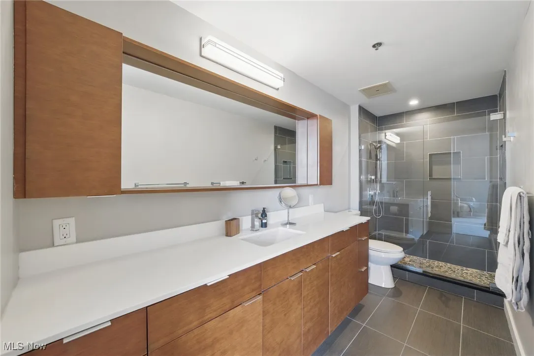 Bathroom featuring toilet, vanity, tile patterned floors, and a stall shower
