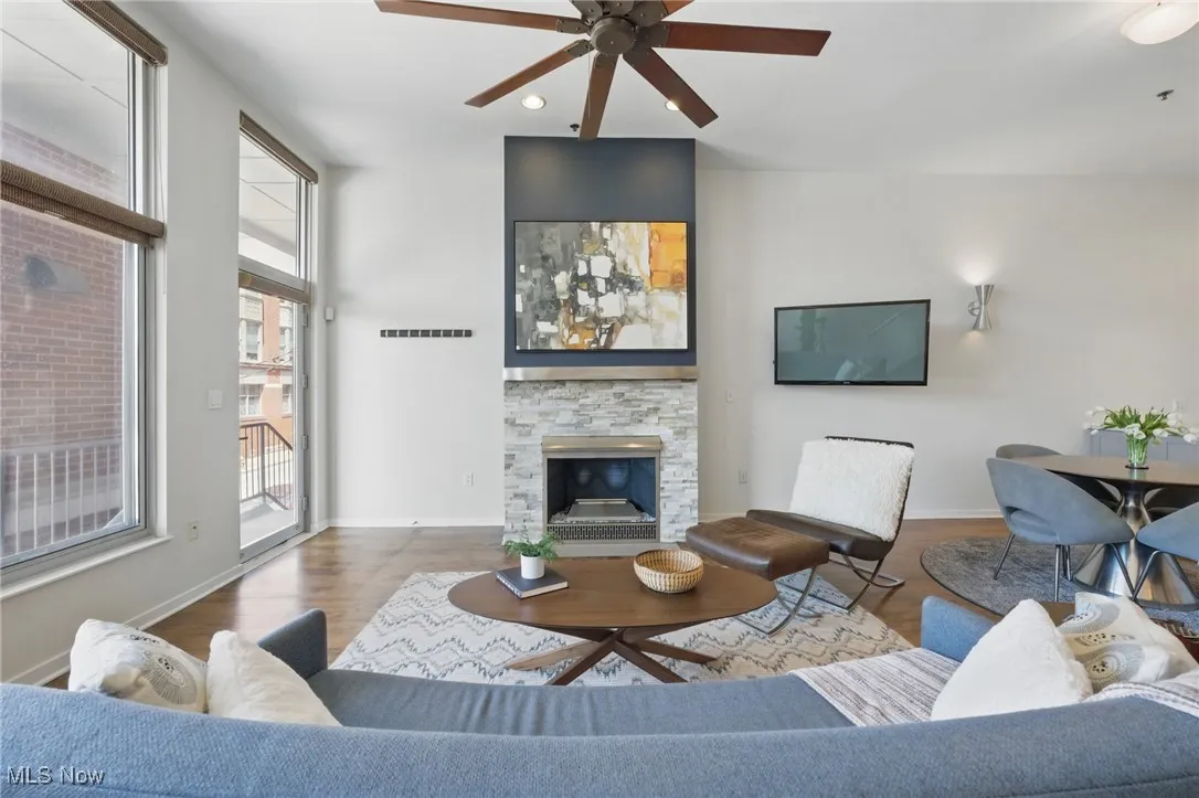 Living room featuring visible vents, baseboards, wood finished floors, ceiling fan, and a stone fireplace