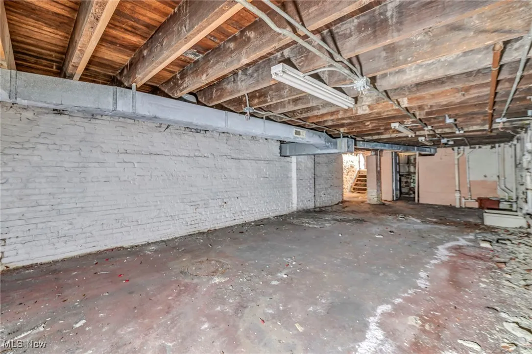 Unfinished basement featuring brick wall and stairs