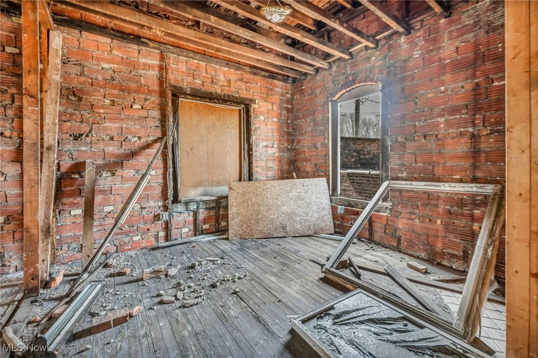 Miscellaneous room with wood-type flooring and brick wall