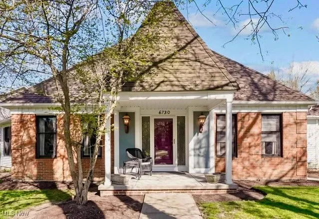View of front of home with a shingled roof, covered porch, and brick siding