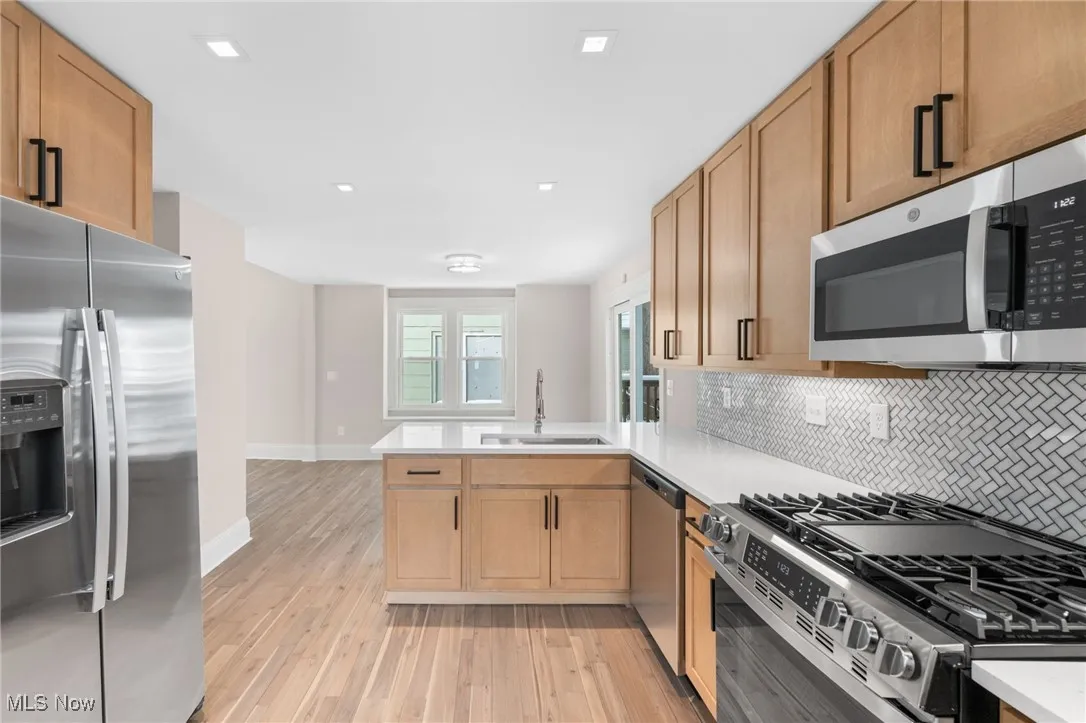 Kitchen with a sink, light countertops, stainless steel appliances, light wood-style flooring, and backsplash