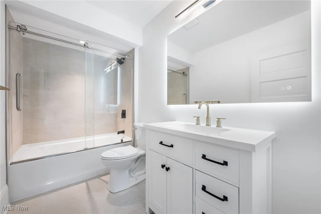 Full bathroom with tile patterned flooring, combined bath / shower with glass door, toilet, and vanity