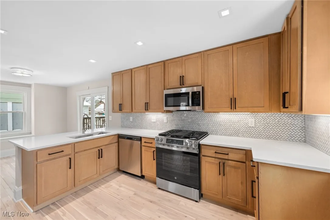 Kitchen featuring a peninsula, a sink, light wood-style floors, and appliances with stainless steel finishes