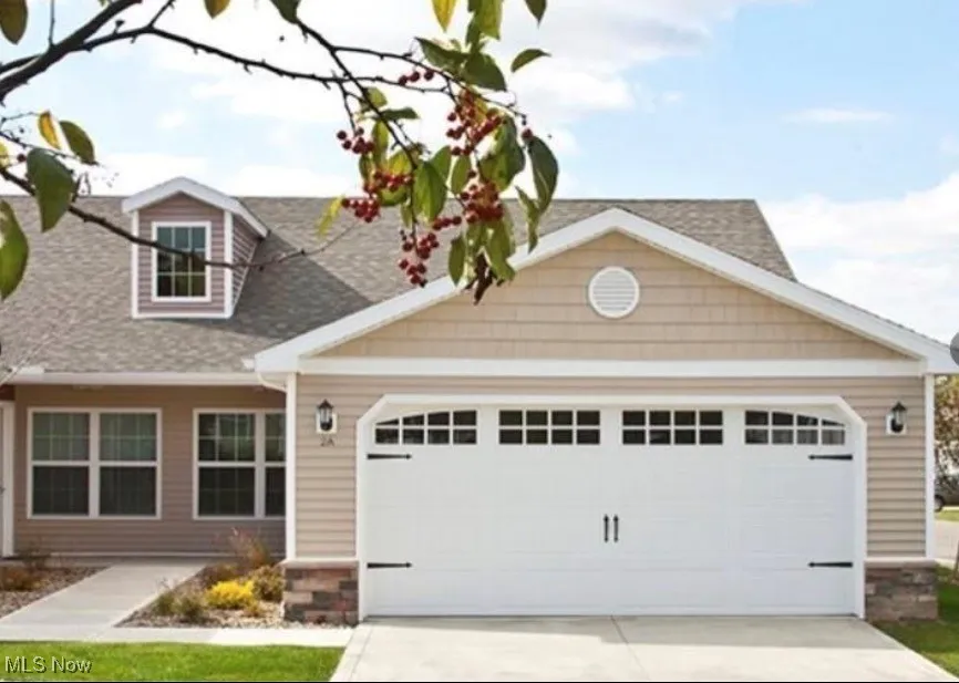 Cape cod-style house featuring concrete driveway, stone siding, an attached garage, and roof with shingles