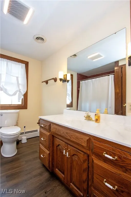 Full bathroom featuring a baseboard heating unit, toilet, visible vents, and wood finished floors