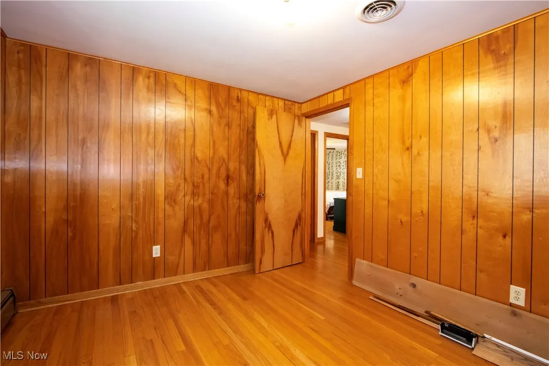 Unfurnished room featuring visible vents, wood finished floors, wooden walls, and a baseboard radiator
