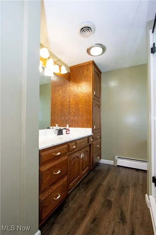 Bathroom featuring vanity, visible vents, baseboards, baseboard heating, and wood finished floors