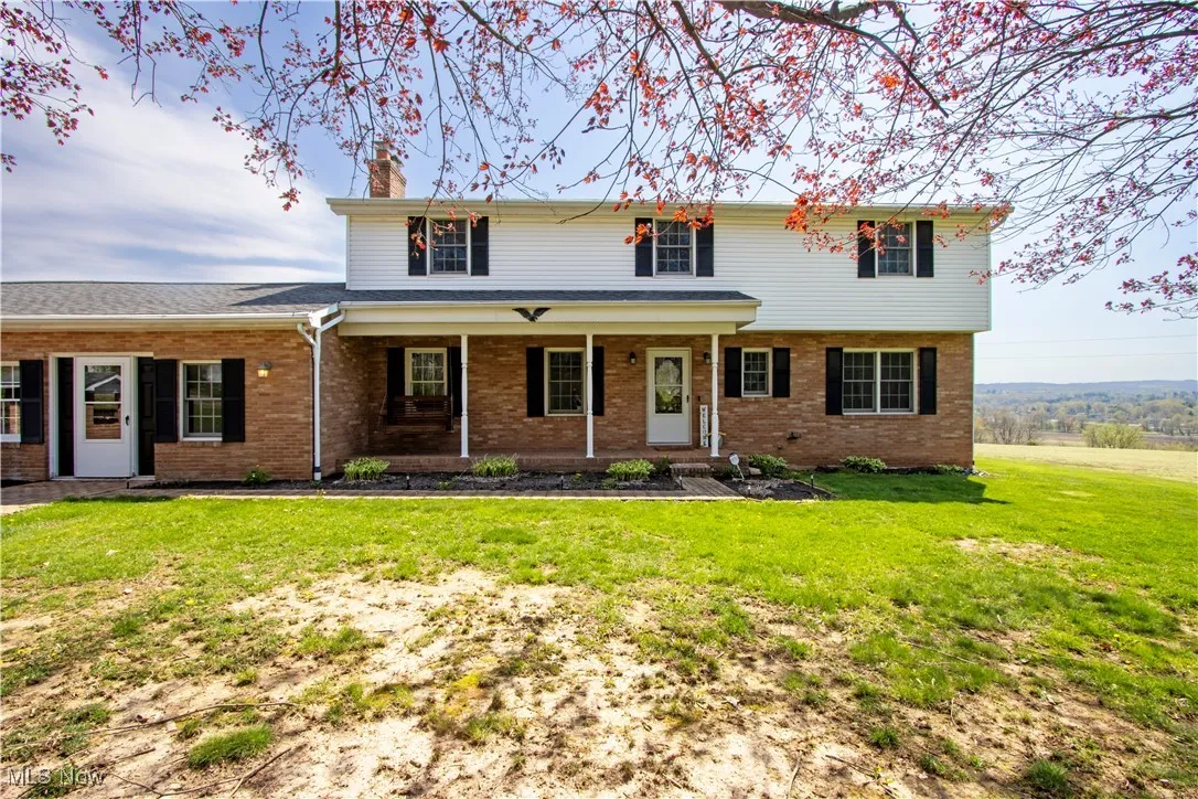 Traditional-style house with a porch, a front lawn, brick siding, and a chimney