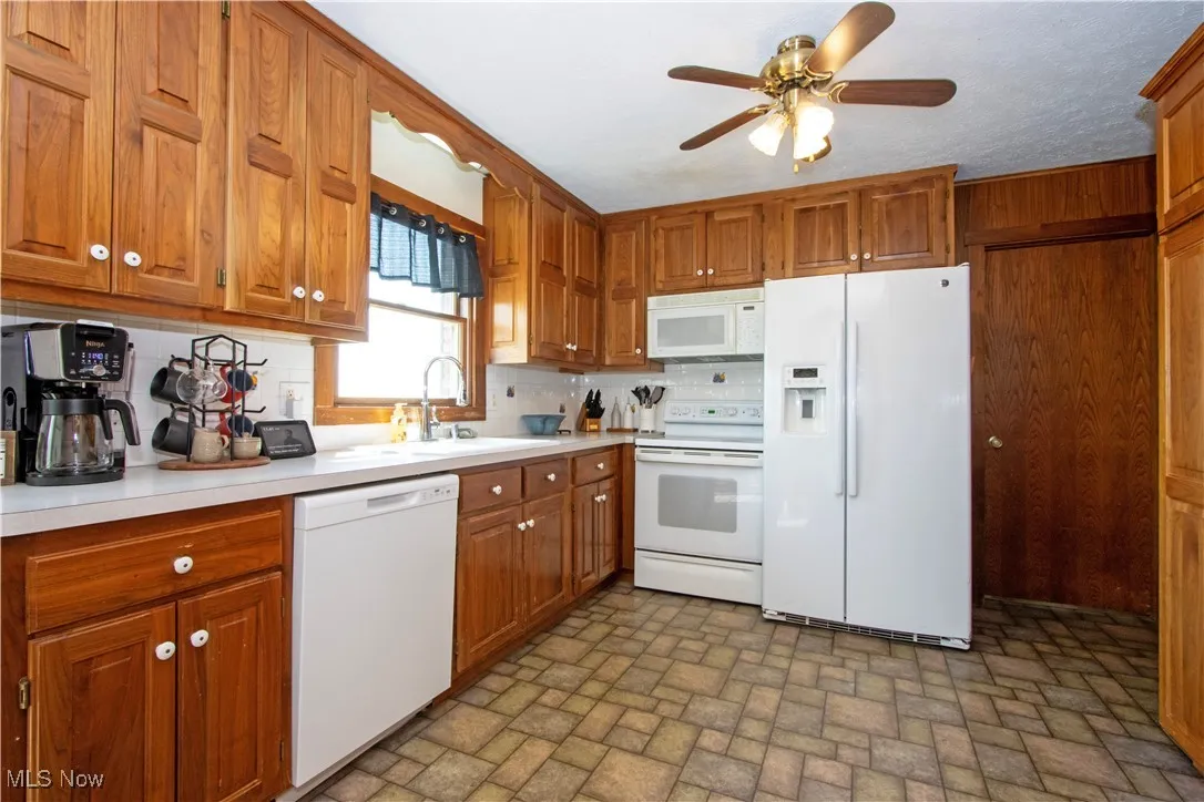 Kitchen featuring brown cabinets, a sink, brick patterned floor, white appliances, and backsplash