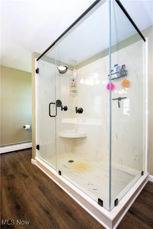 Full bath with a baseboard heating unit, a marble finish shower, and wood finished floors