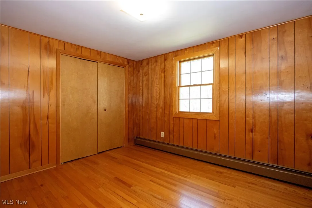 Unfurnished bedroom with a closet, baseboard heating, wood walls, and wood finished floors