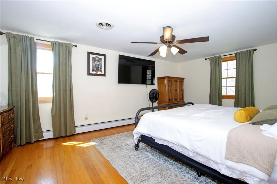Bedroom with a ceiling fan, visible vents, a baseboard radiator, and light wood-style floors