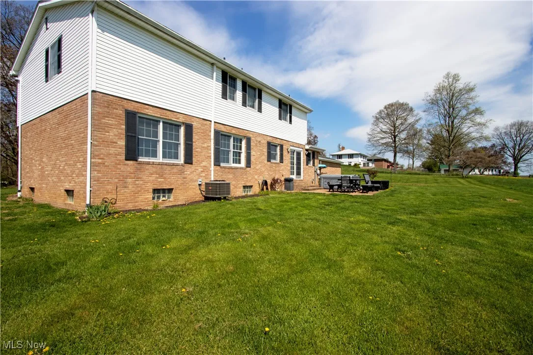 Rear view of house featuring central AC, brick siding, and a lawn