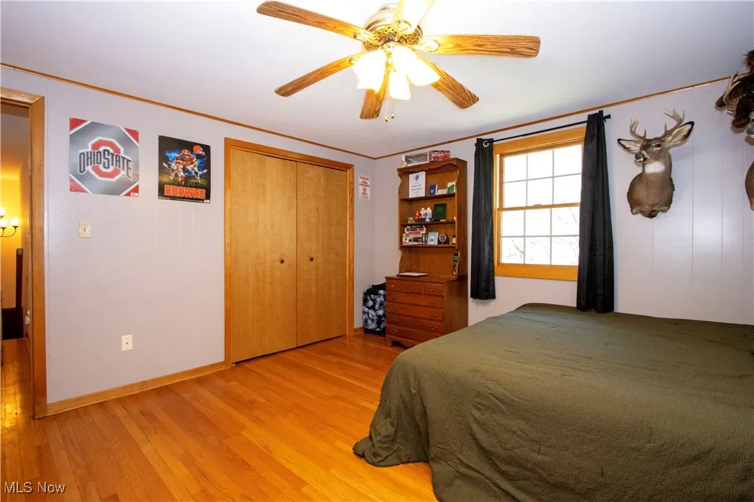 Bedroom featuring a closet, baseboards, light wood-type flooring, a ceiling fan, and crown molding