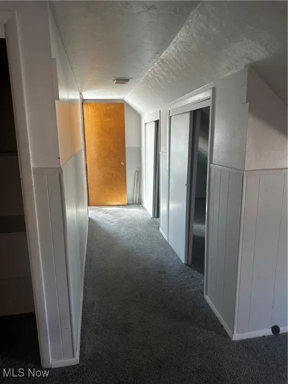 Hall with a textured ceiling, vaulted ceiling, and carpet