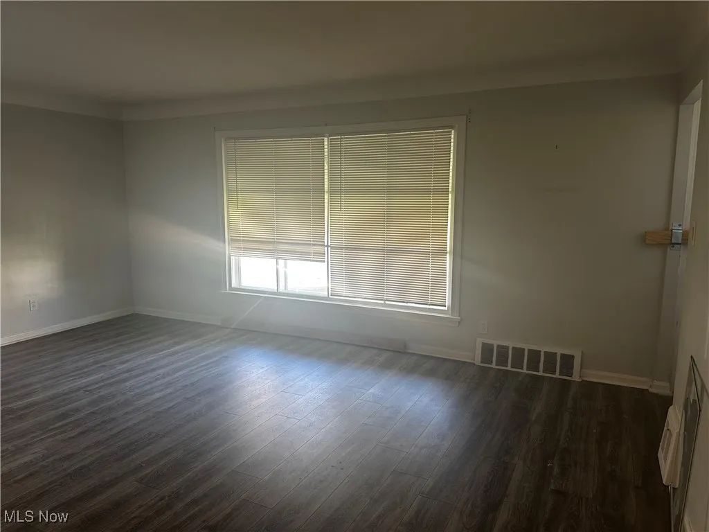 Spare room with dark wood-style floors, visible vents, and baseboards