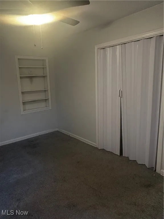 Unfurnished bedroom with baseboards, dark carpet, ceiling fan, and a closet