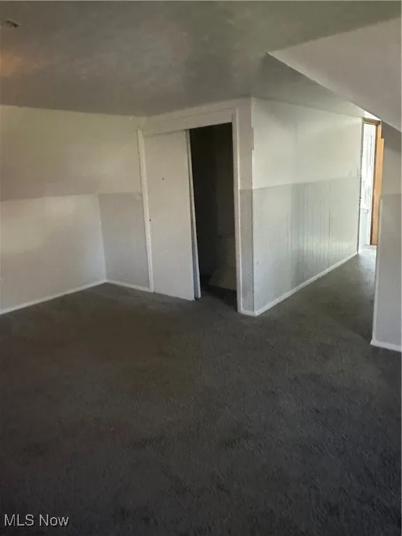 Additional living space featuring dark colored carpet and baseboards
