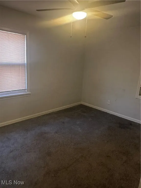 Spare room featuring dark colored carpet, a ceiling fan, and baseboards