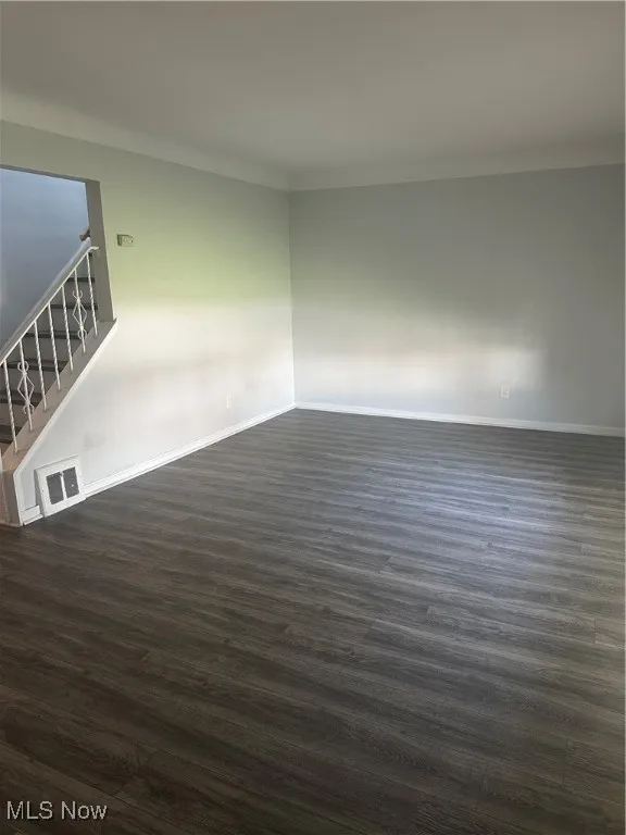 Spare room featuring stairway, visible vents, dark wood-style floors, and baseboards