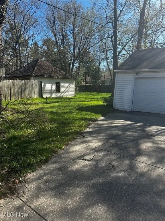 View of yard featuring an outdoor structure, concrete driveway, a garage, and fence