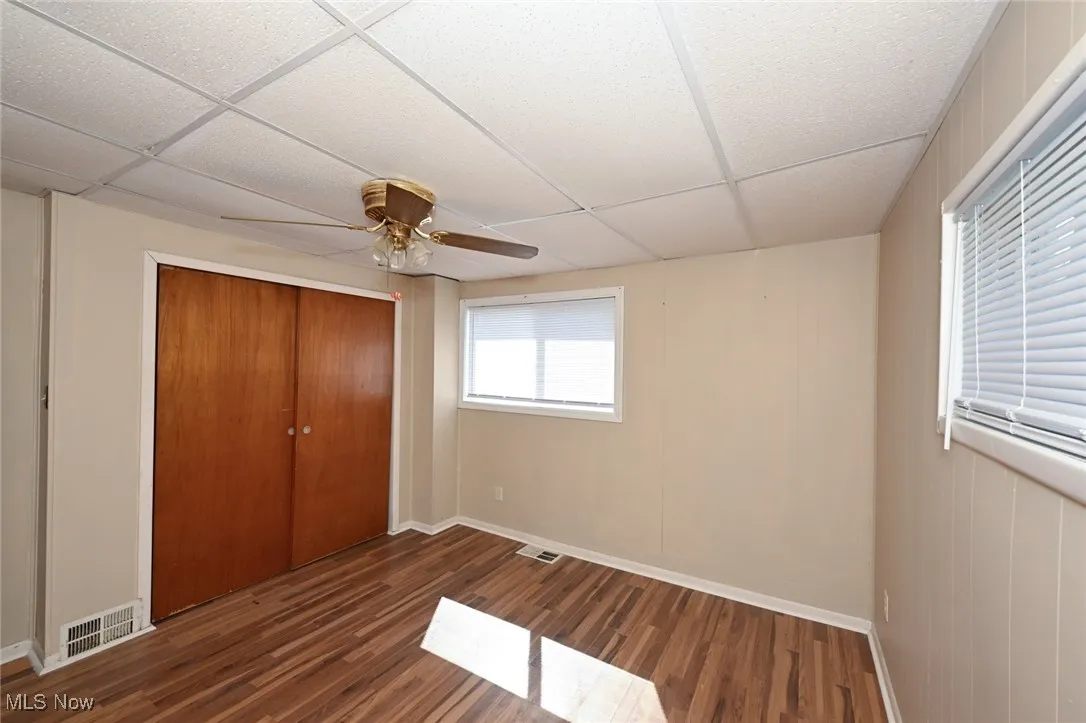Unfurnished bedroom with a paneled ceiling, a closet, visible vents, baseboards, and wood finished floors