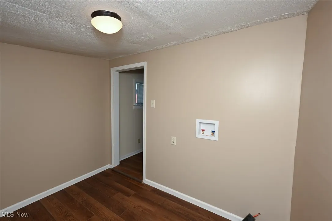 Unfurnished room featuring a textured ceiling, dark wood-style floors, and baseboards