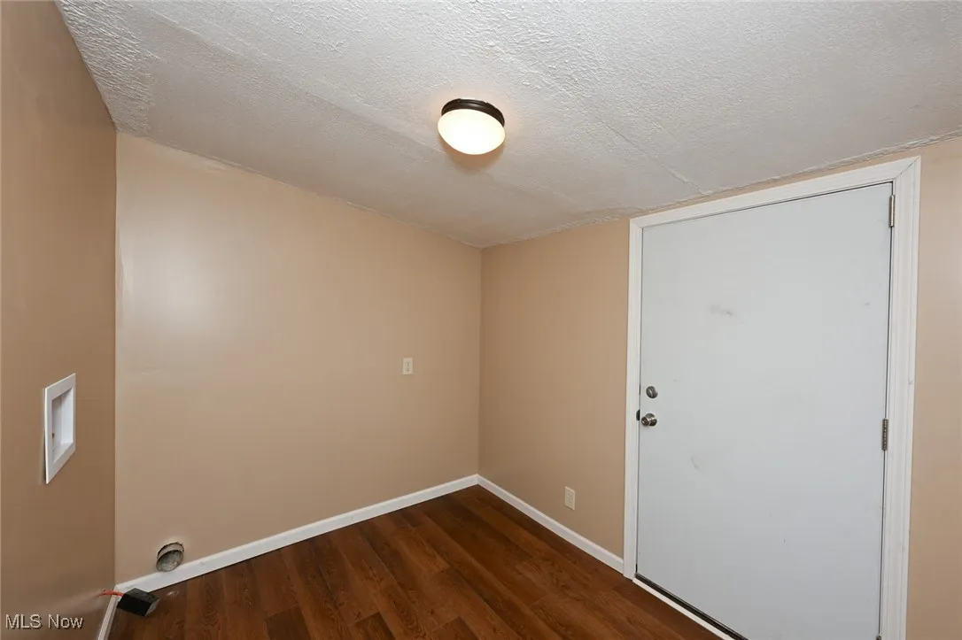 Empty room with a textured ceiling, wood finished floors, and baseboards