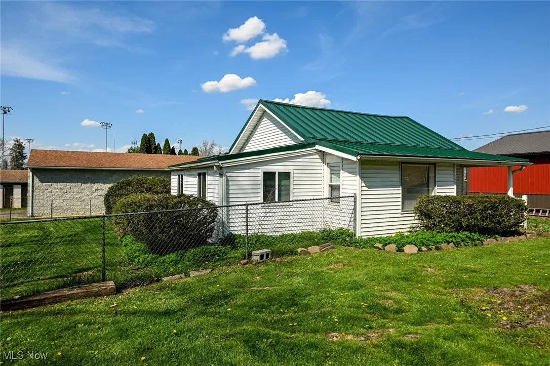 View of side of property featuring fence, a yard, and metal roof