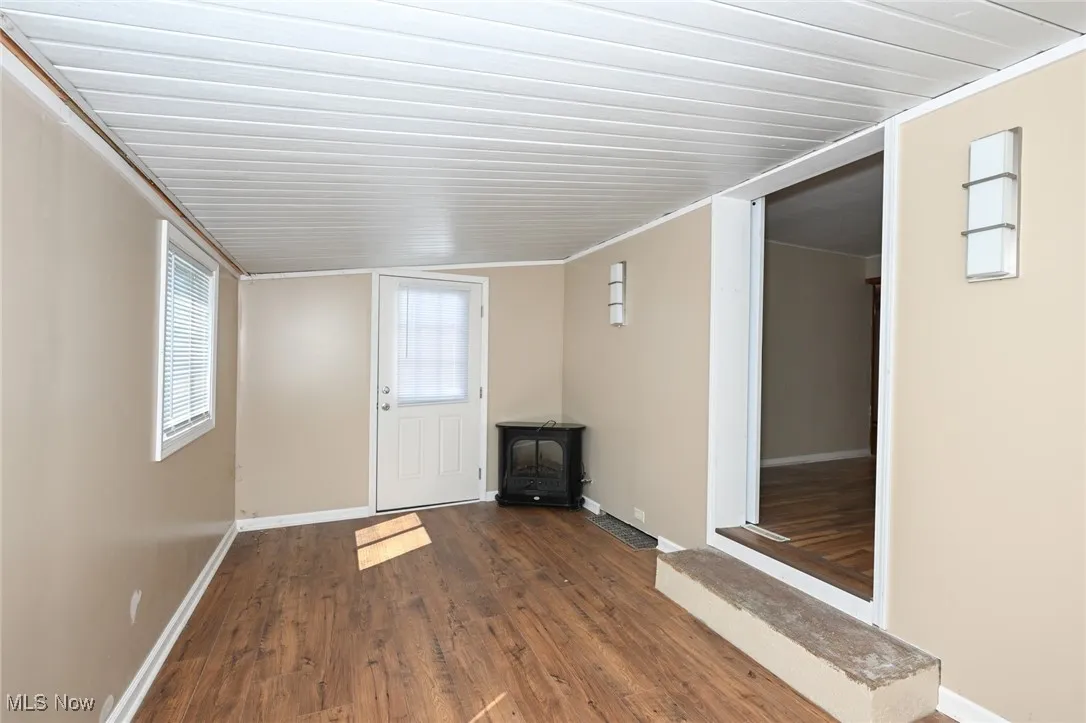 Unfurnished living room with a wood stove, wood finished floors, and baseboards