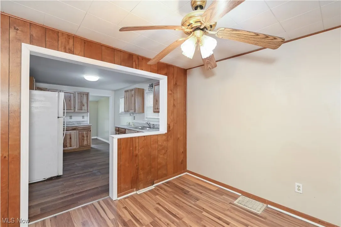 Kitchen featuring brown cabinets, a sink, ceiling fan, freestanding refrigerator, and dark wood-style flooring
