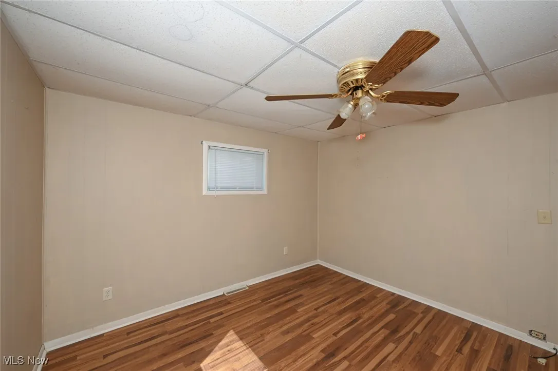 Empty room featuring baseboards, wood finished floors, ceiling fan, and a drop ceiling