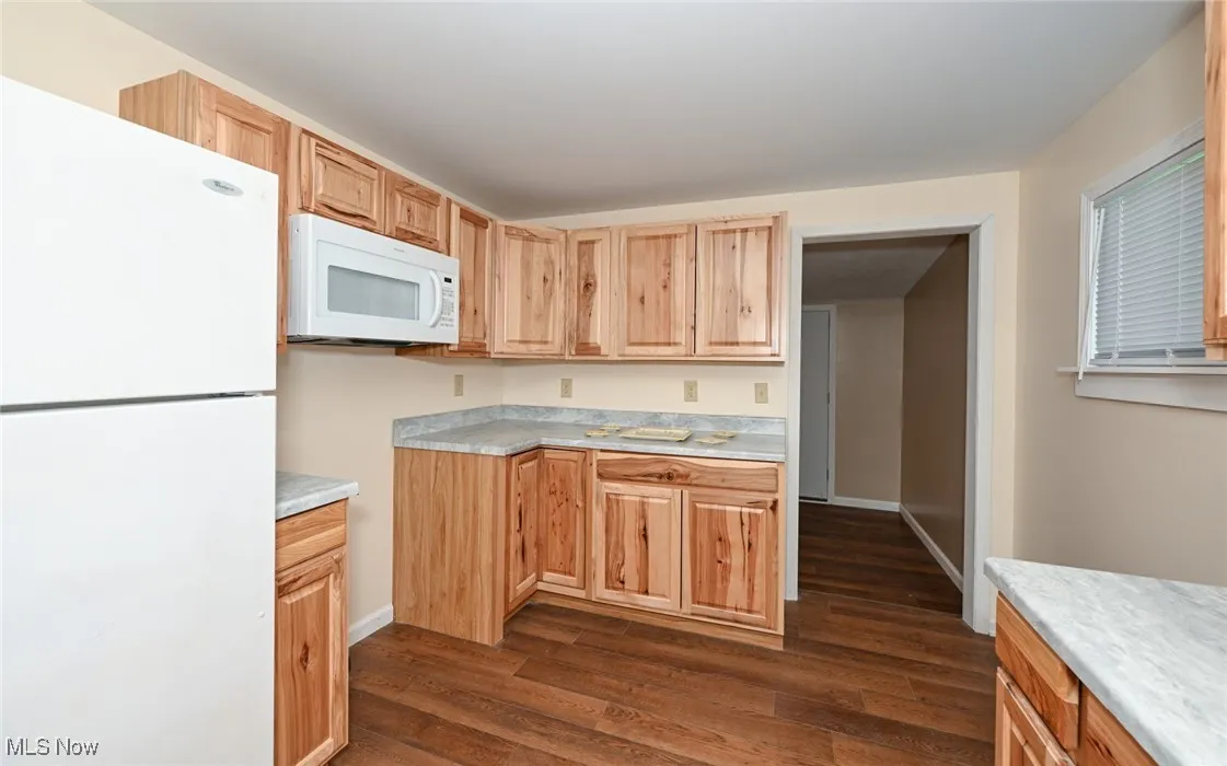 Kitchen featuring dark wood-type flooring, light brown cabinets, white appliances, and light countertops