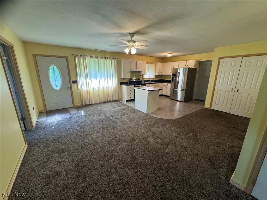 Kitchen with stainless steel fridge, a ceiling fan, open floor plan, dark countertops, and dark colored carpet
