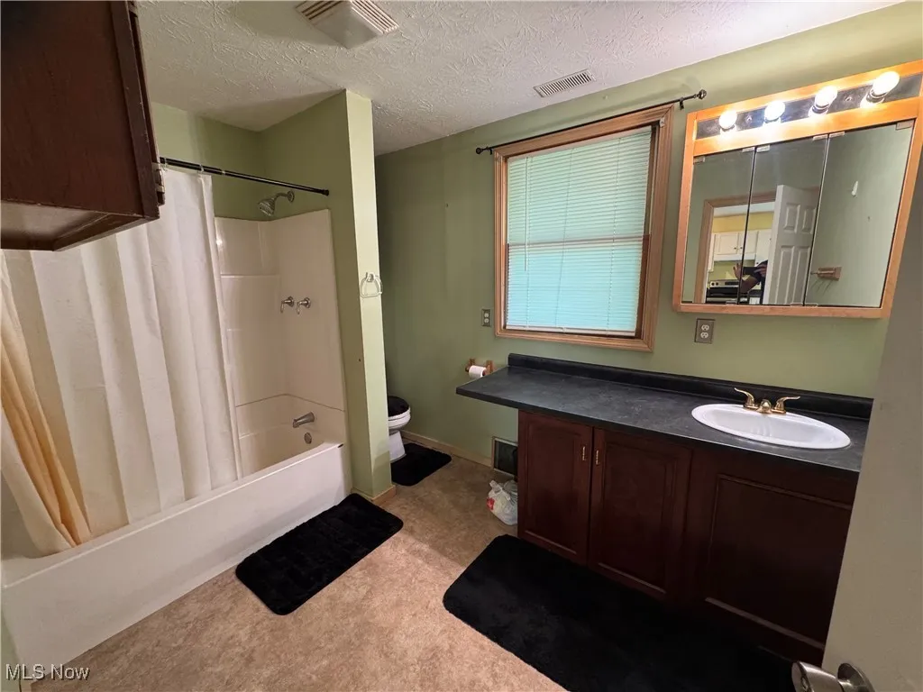 Bathroom with vanity, shower / bathtub combination with curtain, and a textured ceiling