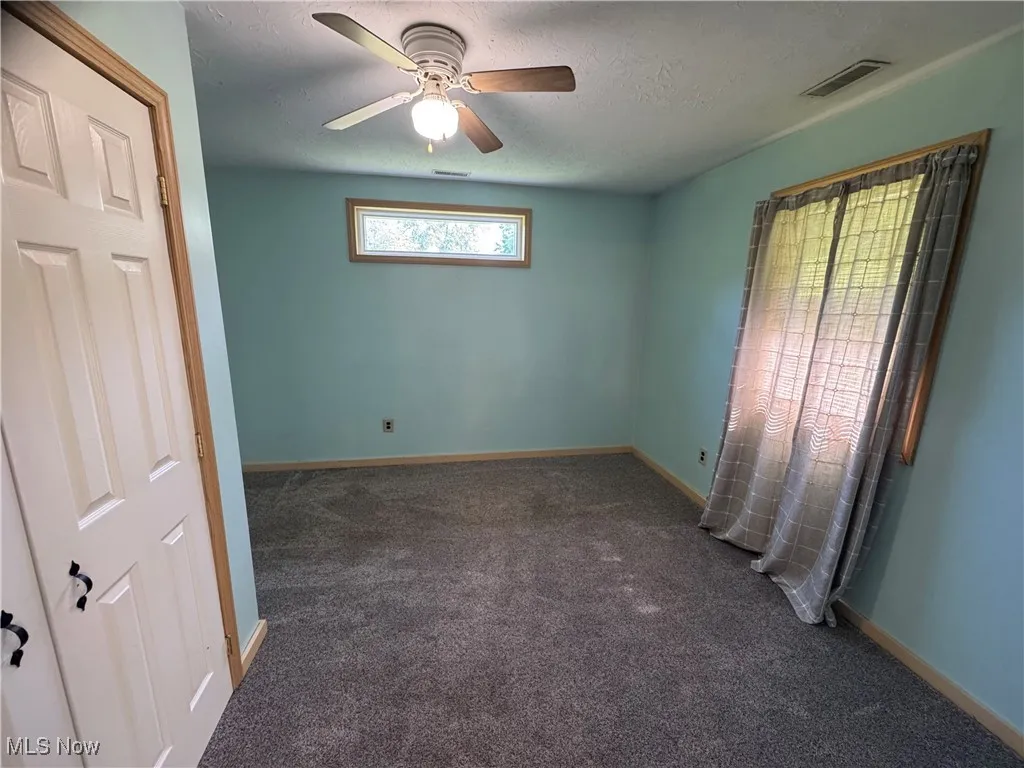 Carpeted empty room with ceiling fan and a textured ceiling