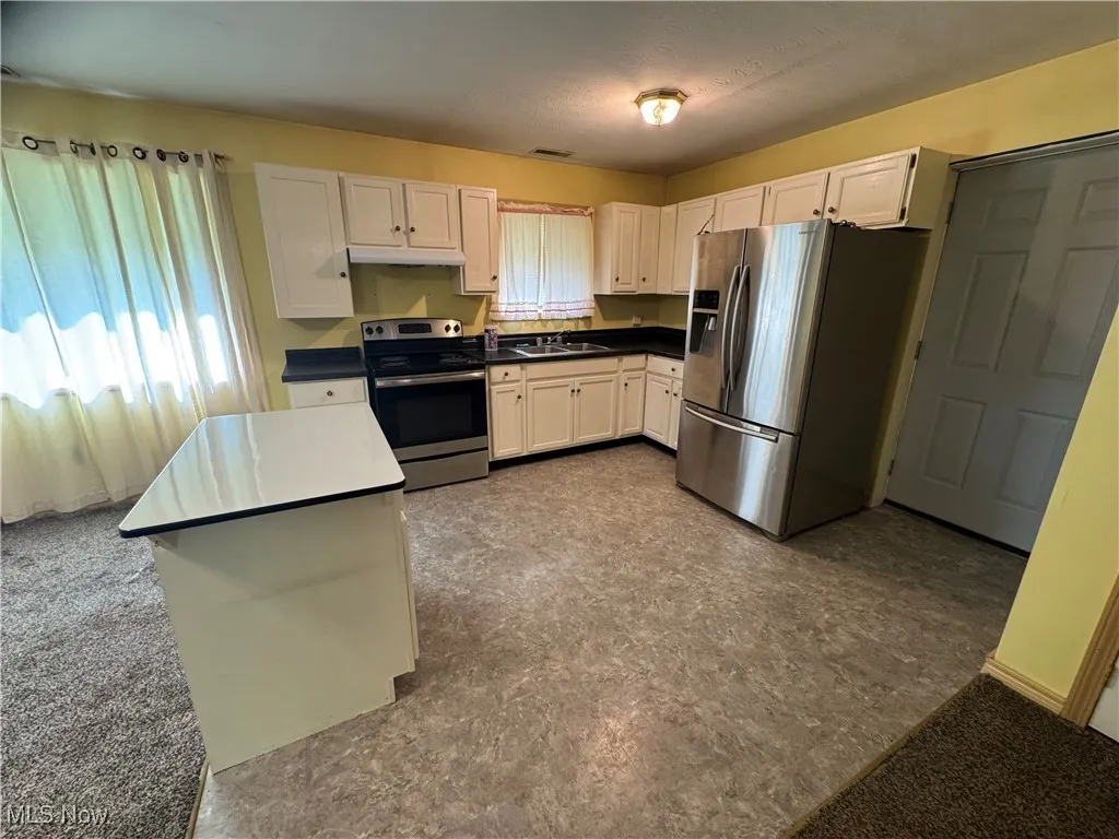 Kitchen with appliances with stainless steel finishes, under cabinet range hood, dark countertops, and white cabinets