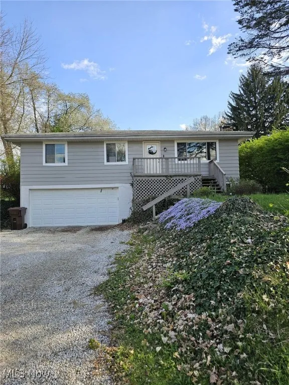 View of front of property featuring a deck, gravel driveway, and a garage