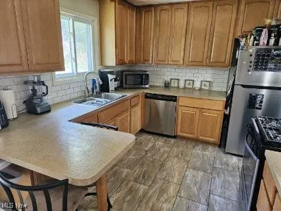 Kitchen with light countertops, a peninsula, appliances with stainless steel finishes, and a sink