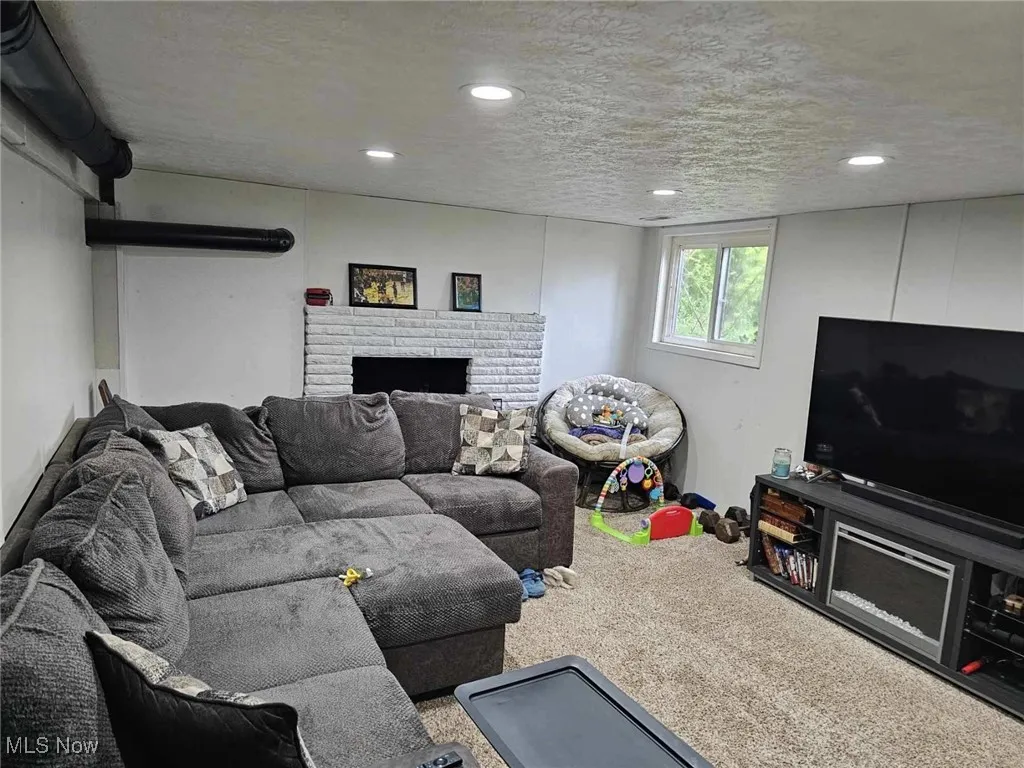 Carpeted living room with a brick fireplace, recessed lighting, and a textured ceiling